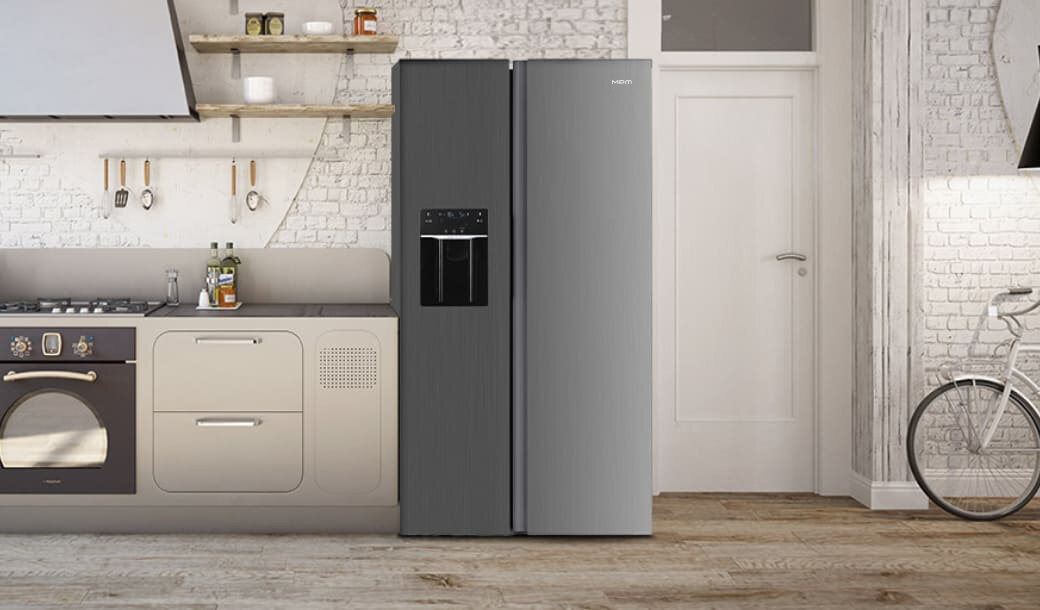 W kuchni znajduje się lodówka side by side w kolorze inox z panelem sterującym i dystrybutorem wody. Obok lodówki widoczna jest zabudowa kuchenna z piekarnikiem i półkami na ścianie.