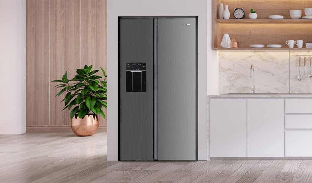Na obrazie widoczna jest nowoczesna lodówka w kolorze inox z panelem sterowania i dystrybutorem wody, umieszczona w eleganckiej kuchni z białymi szafkami i drewnianymi elementami. Obok lodówki stoi roślina w miedzianej donicy.
