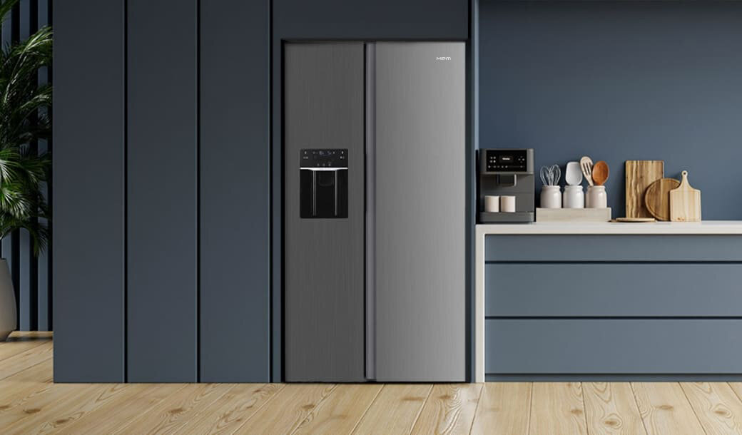 Na obrazie znajduje się nowoczesna kuchnia z lodówką side by side w kolorze inox. Obok lodówki znajduje się blat z ekspres do kawy i akcesoriami kuchennymi.