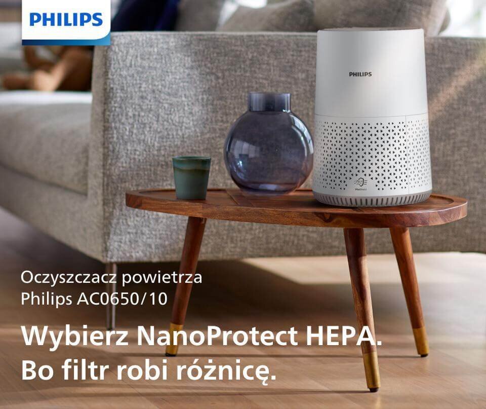 Na drewnianym stoliku stoi oczyszczacz powietrza PHILIPS AC0650/10 obok dwóch wazonów. Tekst na obrazie: \'Oczyszczacz powietrza Philips AC0650/10 Wybierz NanoProtect HEPA. Bo filtr robi różnicę.\'