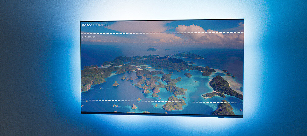 Telewizor wyświetla obraz tropikalnego archipelagu z błękitnym morzem i wyspami, otoczony niebieskim podświetleniem. W lewym górnym rogu widoczny jest tekst \'IMAX ENHANCED\'.