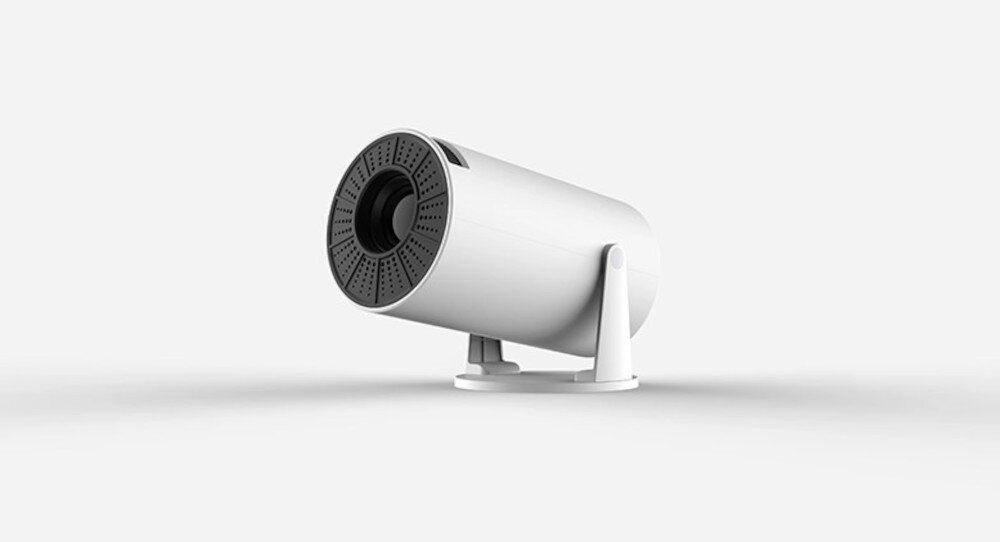 Biały projektor o cylindrycznym kształcie z widocznym obiektywem i perforowaną powierzchnią wokół niego. Urządzenie stoi na dwóch małych nóżkach na jasnym tle.