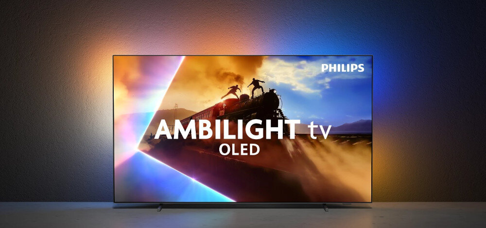 Telewizor wyświetla dynamiczną scenę z pociągiem i postaciami na tle kolorowego nieba. Na ekranie widoczny jest tekst: \'AMBILIGHT tv OLED\', a w rogu logo \'PHILIPS\'.
