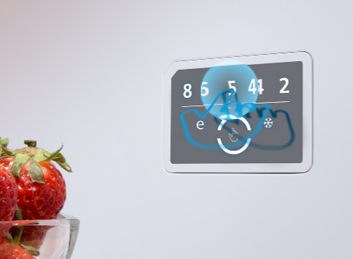 Na białej powierzchni znajduje się panel z cyframi 8, 6, 5, 4, 1, 2 oraz symbolami e i śnieżynki. Obok widoczna jest miska z truskawkami.