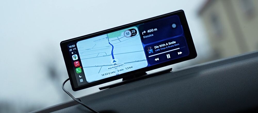 Na zdjęciu widać samochodowy tablet z wyświetlaczem, na którym pokazana jest mapa z trasą oraz odtwarzacz muzyki. Na ekranie widoczne są ikony aplikacji oraz tekst: \'400 m Staszica\' i \'Die With A Smile\'.
