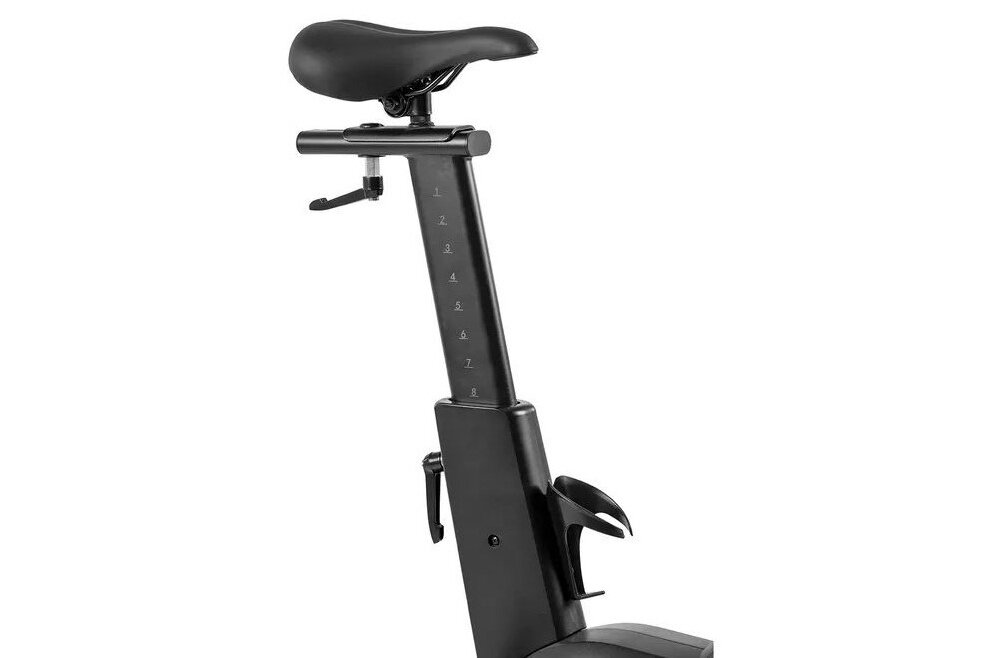 Czarny rower spiningowy z widocznym siodełkiem i regulowaną sztycą z oznaczeniami wysokości. Na sztycy znajduje się uchwyt na bidon.