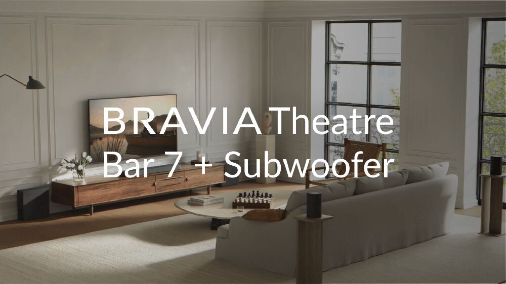 W eleganckim salonie znajduje się telewizor na drewnianej szafce, przed którym stoi jasna sofa. Na obrazie widoczny jest tekst: \'BRAVIA Theatre Bar 7 + Subwoofer\'.