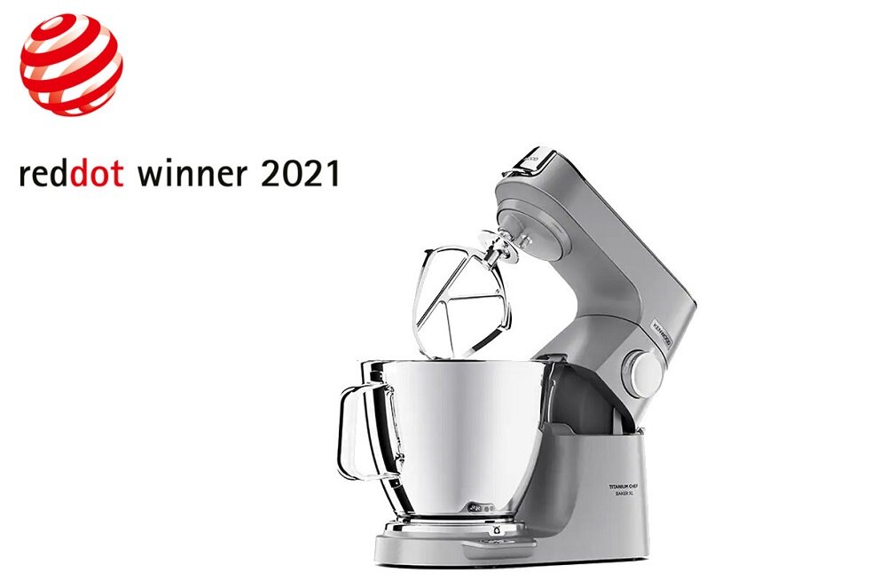 Na obrazie widoczny jest srebrny robot kuchenny z misą i mieszadłem. W lewym górnym rogu znajduje się logo Red Dot oraz tekst \'reddot winner 2021\'.