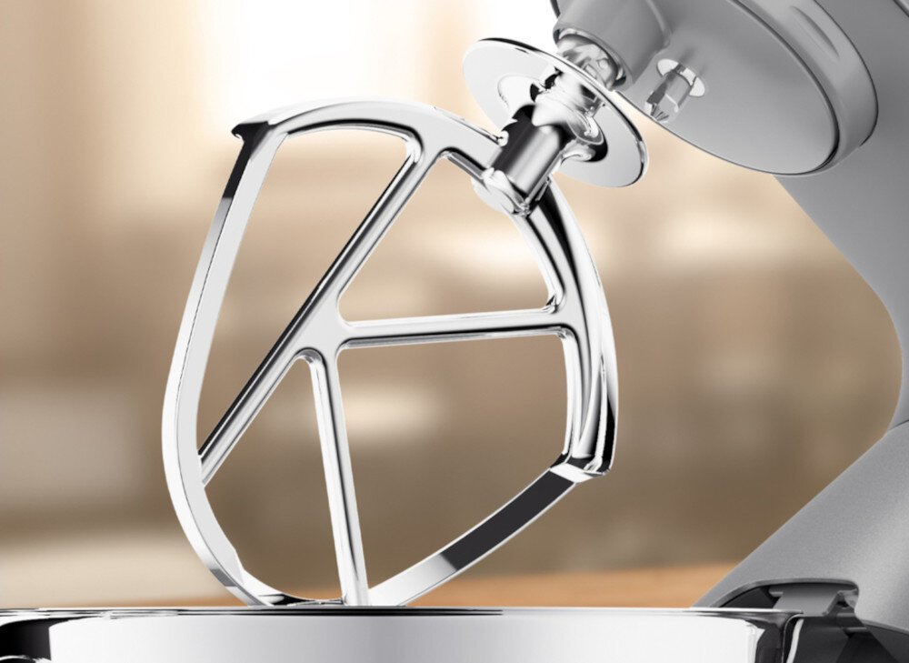 Na zdjęciu widoczny jest metalowy mieszadło planetarnego robota kuchennego, zamocowane w urządzeniu. Tło jest rozmyte, co podkreśla szczegóły mieszadła.