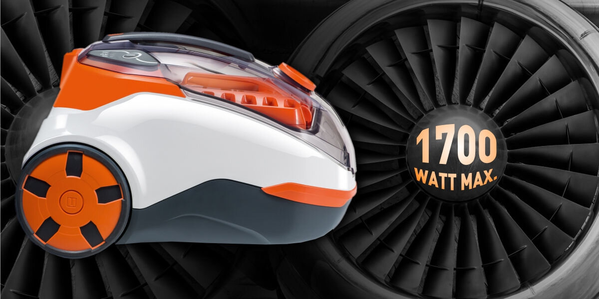 Obraz przedstawia odkurzacz w kolorach białym, pomarańczowym i szarym, z widocznymi kołami. W tle znajduje się turbina z napisem \'1700 WATT MAX.\'.