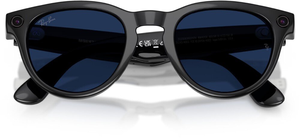 Czarne okulary przeciwsłoneczne z ciemnymi soczewkami i logo \'Ray-Ban\' na jednym z zauszników. Na wewnętrznej stronie zausznika widoczne są oznaczenia i symbole certyfikacyjne.