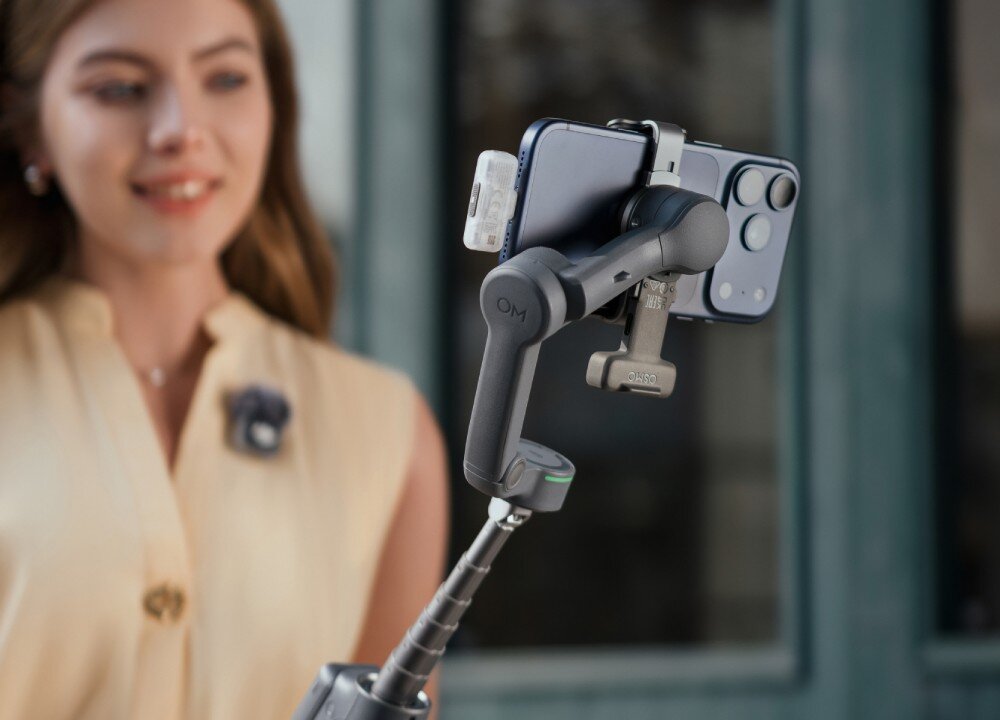 Moduł wielofunkcyjny DJI do Osmo Mobile 8P Zbliżenie na tylną część szarego stabilizatora z zamocowanym smartfonem, który znajduje się na rozłożonym wysięgniku. W porcie telefonu umieszczone jest małe, szare urządzenie zewnętrzne, przeznaczenie, kompatybilność, działanie