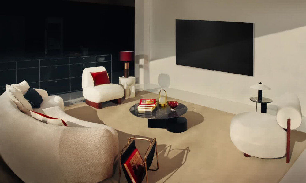 Nowoczesny salon z telewizorem zamontowanym na ścianie. W pomieszczeniu znajdują się eleganckie meble, w tym kanapa, fotele i stolik z książkami oraz dekoracjami.