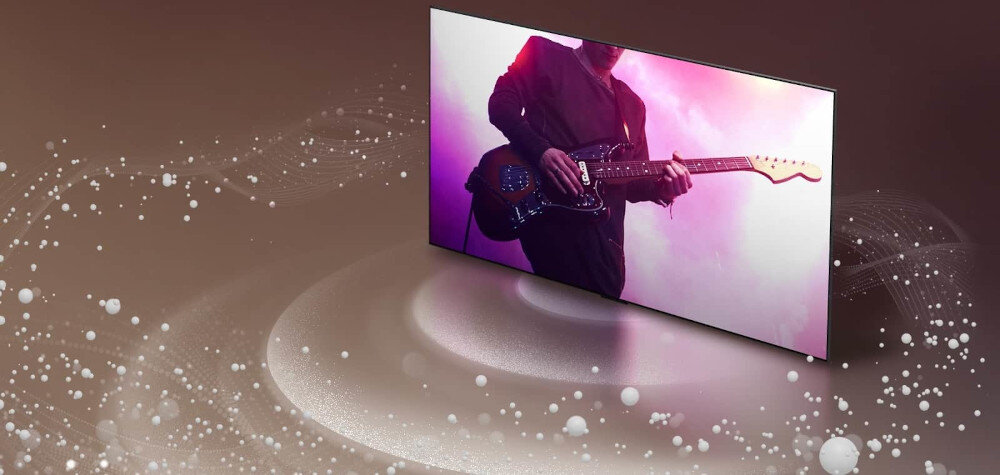 Telewizor wyświetla obraz osoby grającej na gitarze elektrycznej w otoczeniu różowego światła. W tle widoczne są efekty graficzne przypominające fale dźwiękowe i unoszące się białe kuleczki.