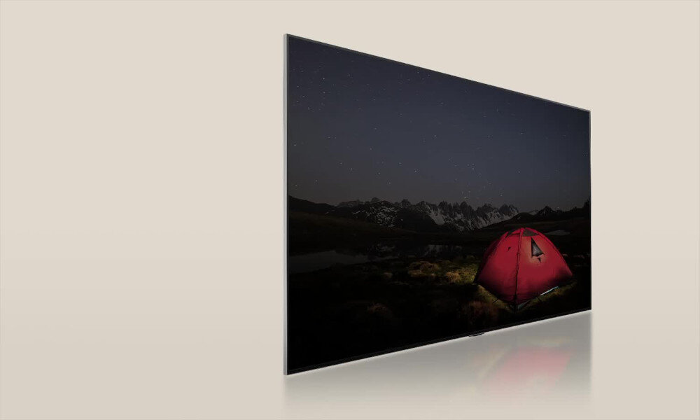 Telewizor wyświetla obraz nocnego krajobrazu z czerwonym namiotem na tle gór i gwiaździstego nieba. Ekran jest cienki i ma nowoczesny design.