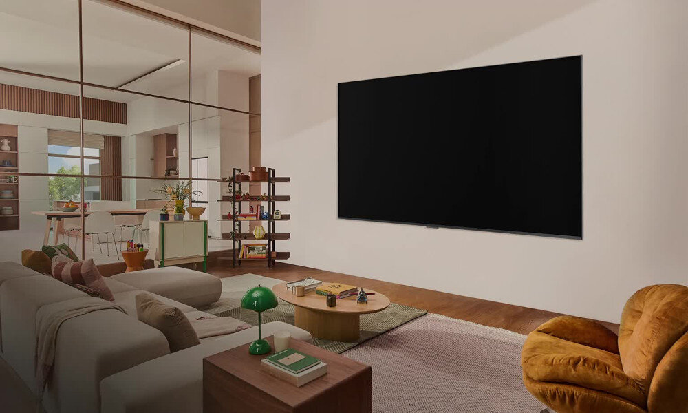 W przestronnym salonie na ścianie wisi duży telewizor z czarnym ekranem. W pomieszczeniu znajdują się także kanapa, stolik kawowy i fotel.