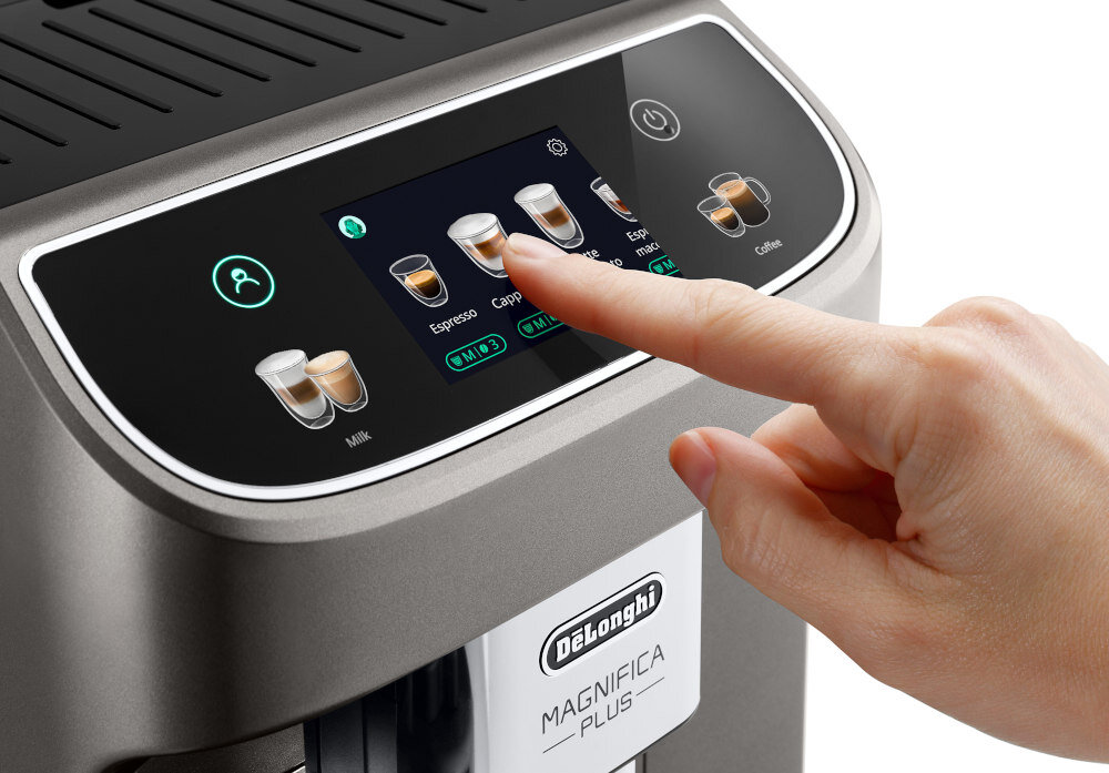 Osoba dotyka ekranu dotykowego ekspresu do kawy, na którym widoczne są opcje napojów, takie jak Espresso i Cappuccino. Na obudowie znajduje się logo \'DeLonghi Magnifica Plus\'.