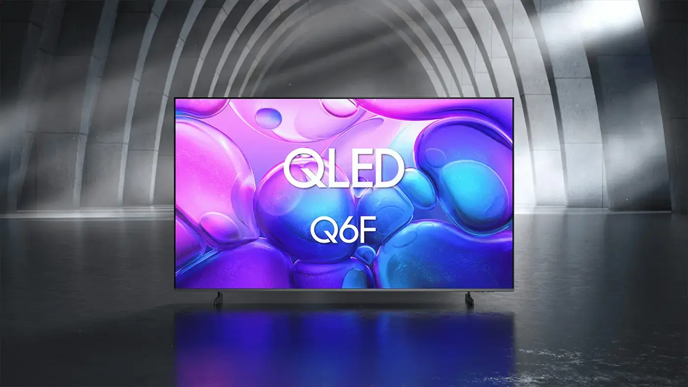 Telewizor z wyświetlaczem pokazującym kolorowe, abstrakcyjne wzory w odcieniach fioletu i niebieskiego z widocznym napisem \'QLED Q6F\'. W tle znajduje się ciemne, łukowate wnętrze z padającym światłem.
