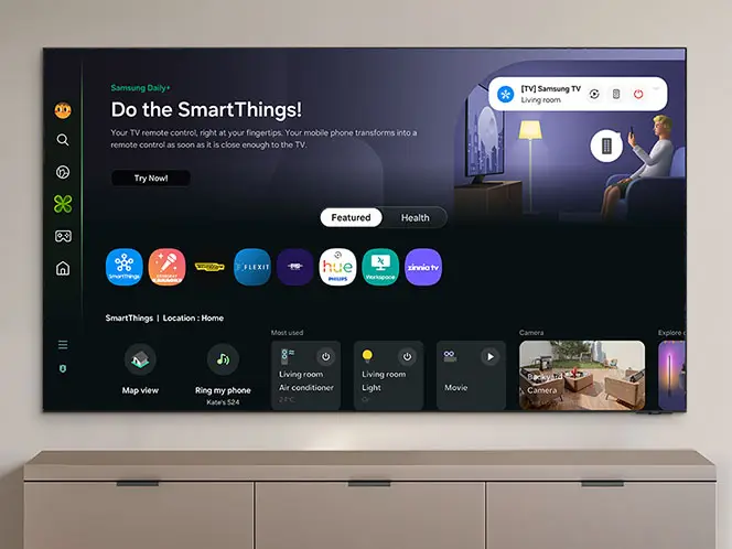 Telewizor wyświetla interfejs SmartThings z różnymi aplikacjami i opcjami sterowania. Na ekranie widoczny jest tekst: \'Do the SmartThings!\' oraz ikony aplikacji takie jak Map view, Ring my phone, Living room Air conditioner.