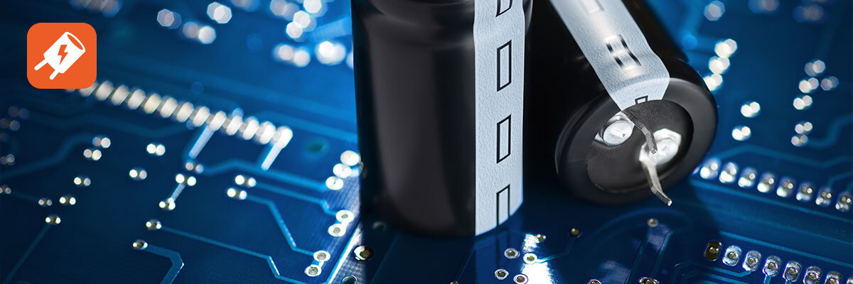 Obraz przedstawia zbliżenie na niebieską płytkę drukowaną z widocznymi ścieżkami i elementami elektronicznymi. W lewym górnym rogu znajduje się pomarańczowa ikona z białym symbolem błyskawicy i wtyczki.