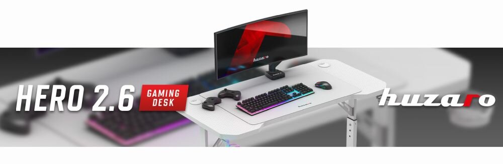 Obraz przedstawia białe biurko gamingowe z monitorem, klawiaturą, myszką i dwoma kontrolerami. Na obrazie widoczny jest tekst: \'HERO 2.6 GAMING DESK\' oraz logo \'huzaro\'.