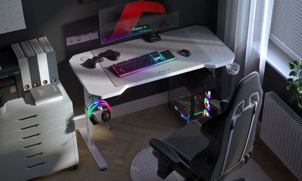 Na obrazie znajduje się biurko gamingowe z białym blatem, na którym umieszczono monitor, klawiaturę z podświetleniem RGB, myszkę oraz słuchawki. Obok biurka stoi czarne krzesło gamingowe, a pod biurkiem znajduje się komputer z podświetleniem RGB.