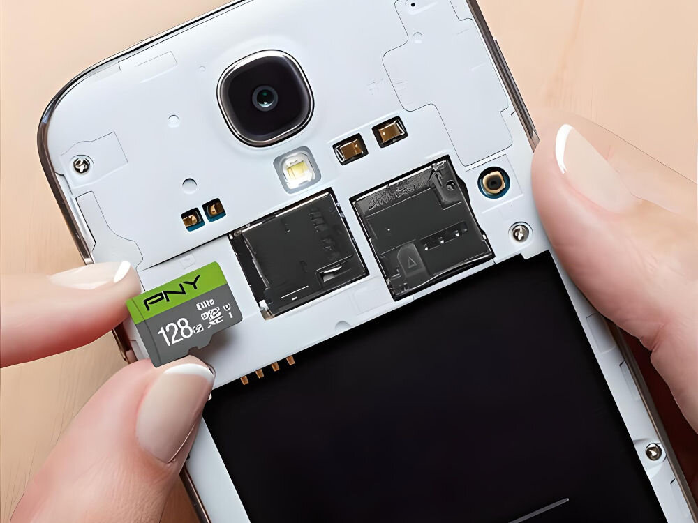 Osoba wkłada kartę pamięci PNY microSDXC Elite 128GB do otwartego slotu w telefonie. Na karcie widoczny jest napis \'PNY 128GB\'.