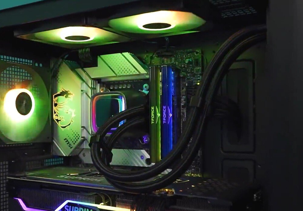 Wnętrze komputera z widocznym chłodzeniem wodnym i podświetleniem RGB. Na płycie głównej znajduje się logo MSI oraz napisy \'T-FORCE\' na pamięciach RAM.