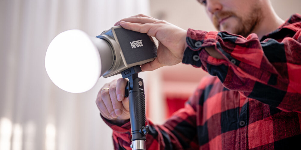 LAMPA LED NEWELL ZORA 60 WB (2700 - 6500 K) Osoba trzyma świecącą lampę LED Newell z zamontowanym silikonowym dyfuzorem i reguluje jej ustawienie za pomocą uchwytu