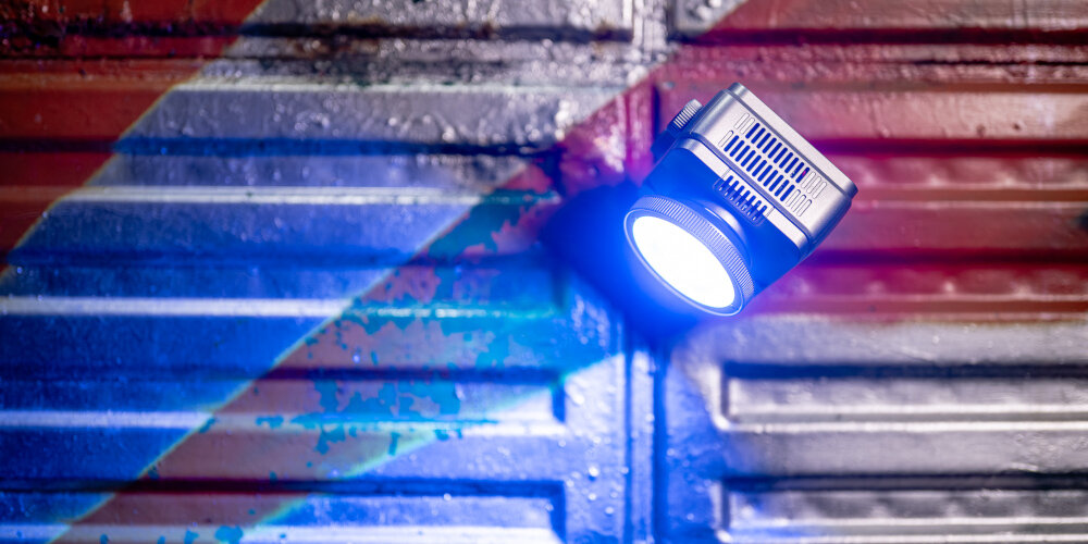 LAMPA LED NEWELL ZORA MINI 40 RGB Świecąca lampa LED z dyfuzorem jest przymocowana do metalowej powierzchni, oświetlając kolorowe, industrialne tło