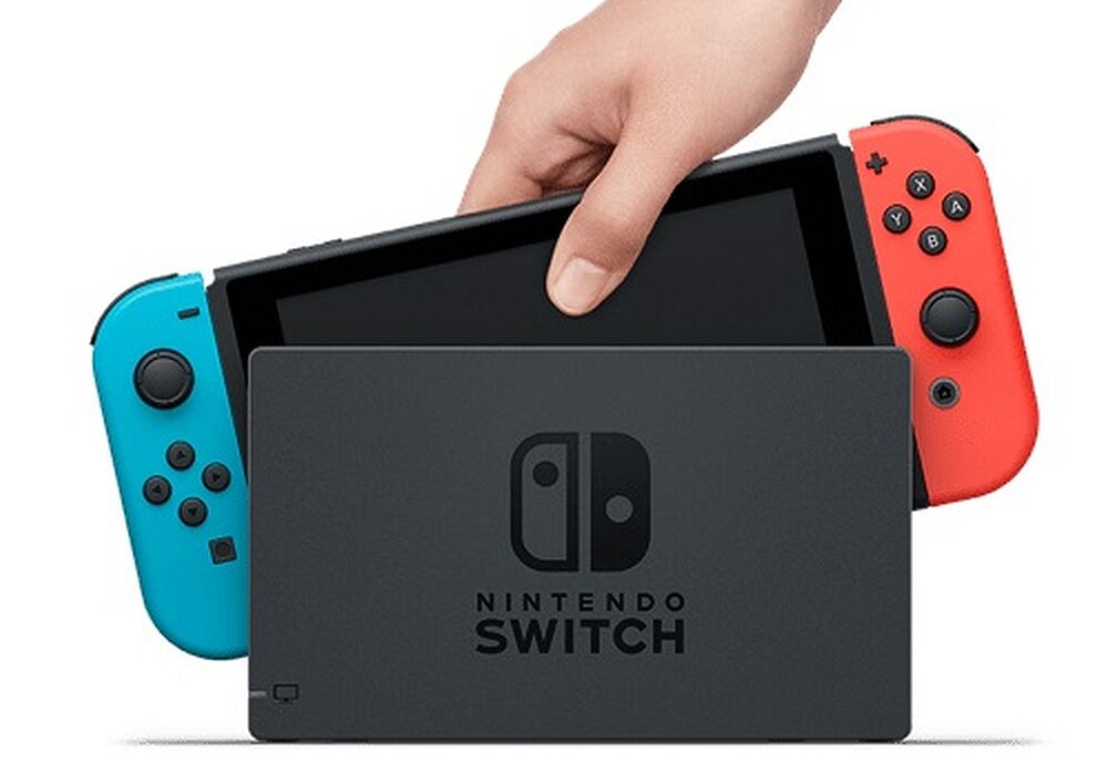 Konsola z ekranem dotykowym jest wkładana do stacji dokującej, z kontrolerami w kolorach niebieskim i czerwonym. Na stacji dokującej widoczne jest logo \'NINTENDO SWITCH\'.