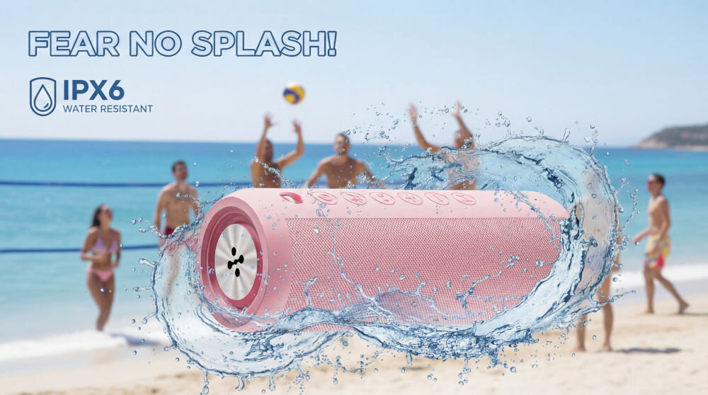 Różowy głośnik mobilny unosi się na fali wody na tle plaży z ludźmi grającymi w siatkówkę. Na obrazie widoczny jest tekst: \'FEAR NO SPLASH!\' oraz \'IPX6 WATER RESISTANT\'.