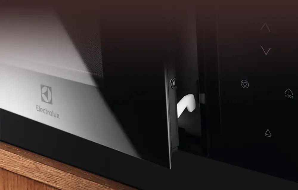 Zbliżenie na panel sterowania czarnej kuchenki mikrofalowej z widocznym logo Electrolux. Na panelu znajdują się przyciski dotykowe z symbolami strzałek i funkcji +30s.