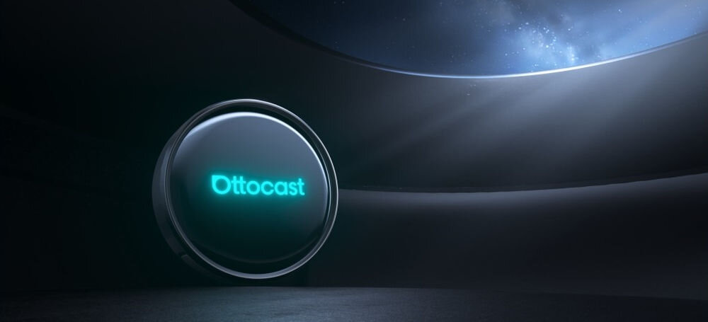 Na obrazie widoczny jest okrągły, czarny obiekt z napisem \'Ottocast\' w jasnym kolorze. W tle znajduje się ciemne, futurystyczne wnętrze z widocznym fragmentem nieba.