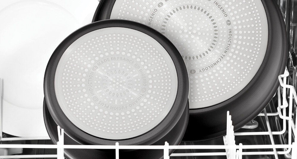 Dwa czarne garnki z metalowymi spodami umieszczone w zmywarce. Na spodach widoczny jest tekst: \'MADE IN FRANCE\', \'INGENIO\', \'INDUCTION TECHNOLOGY\'.