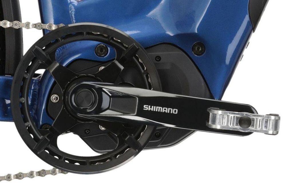 Zbliżenie na mechanizm korbowy roweru w kolorze niebiesko-czarnym z widocznym napisem \'SHIMANO\' na ramieniu korby.