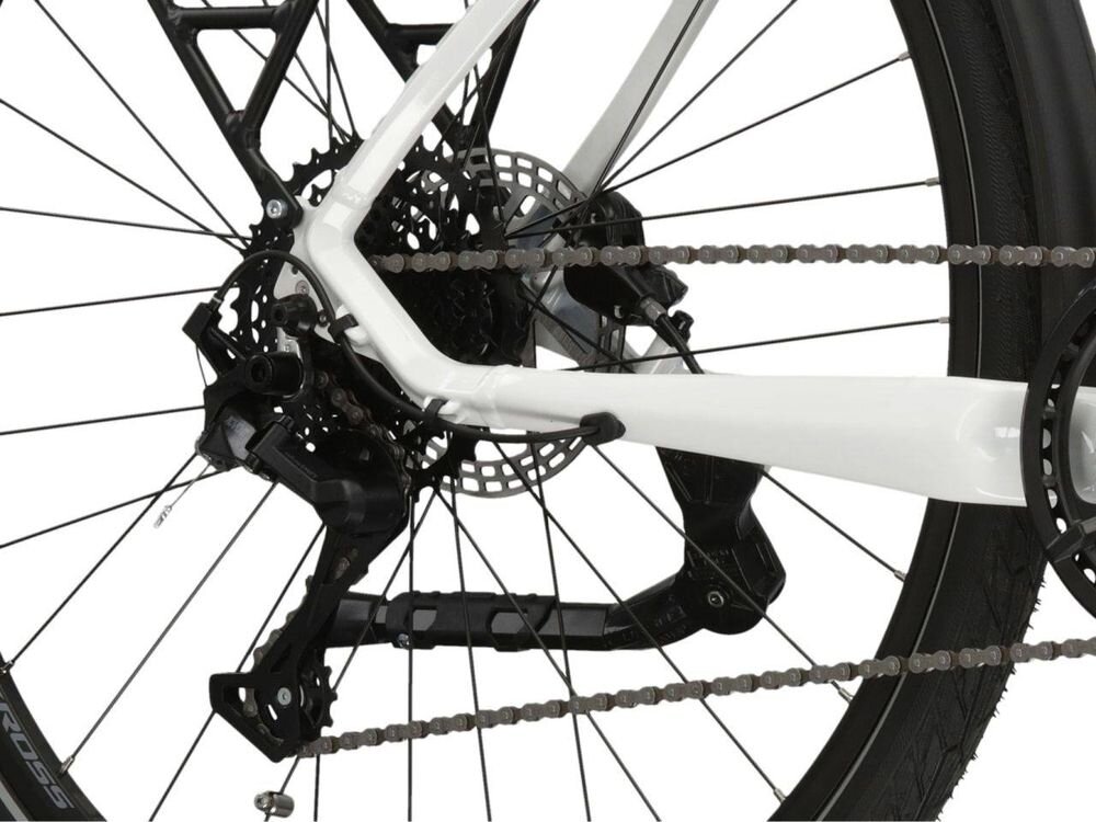 Zbliżenie na tylne koło roweru z widocznym mechanizmem przerzutki i tarczą hamulcową. Rama roweru jest w kolorze biało-srebrnym.