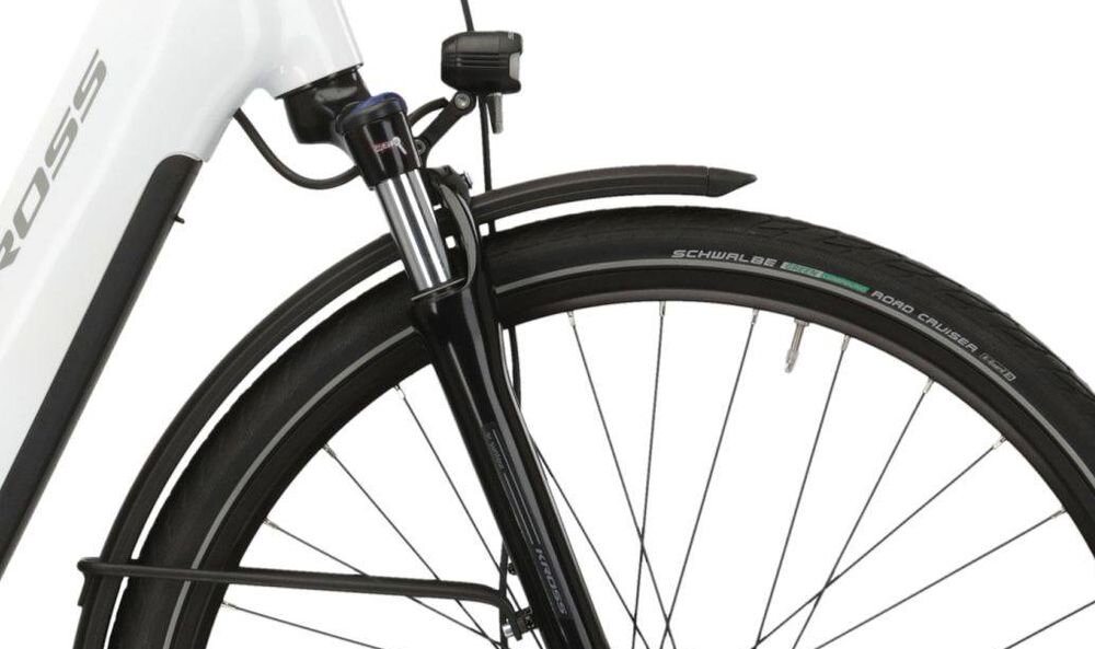 Zbliżenie na przednie koło roweru z widocznym amortyzatorem i błotnikiem. Na oponie widoczny jest napis \'SCHWALBE Road Cruiser Plus\'.