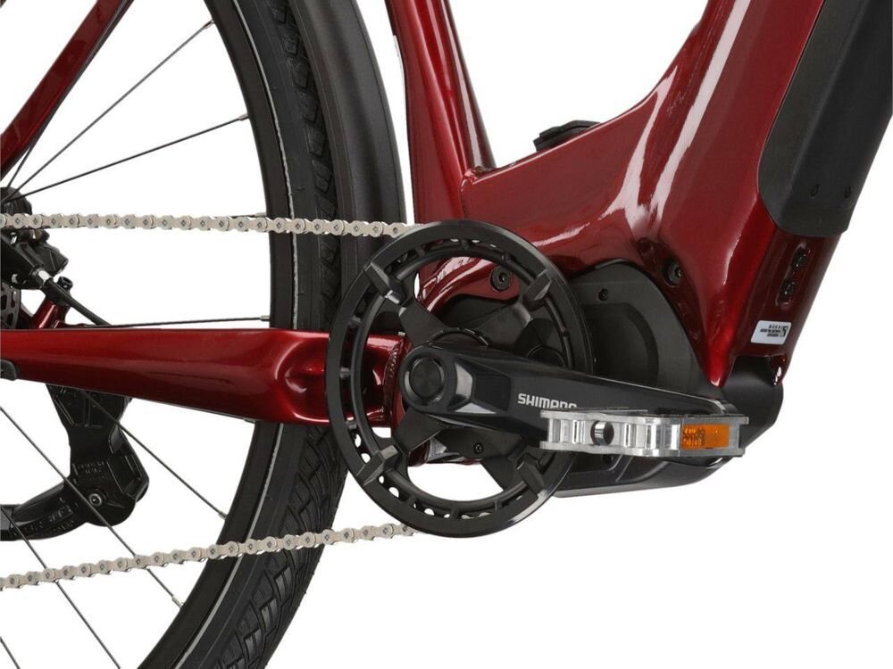 Zbliżenie na mechanizm napędowy roweru elektrycznego w kolorze rubinowym, z widocznym logo Shimano na korbie.