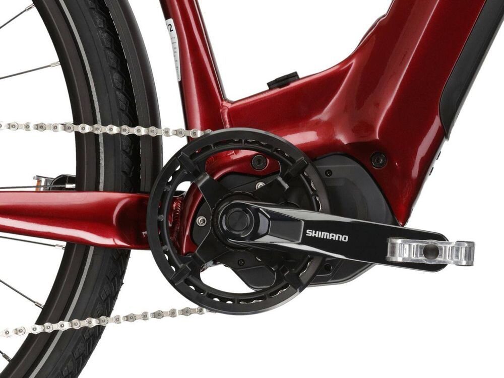 Zbliżenie na mechanizm korbowy roweru w kolorze rubinowym z widocznym napisem \'SHIMANO\' na ramieniu korby.