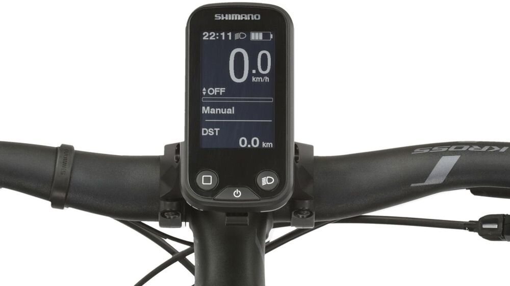 Na zdjęciu widoczny jest wyświetlacz roweru elektrycznego z logo \'SHIMANO\', pokazujący prędkość 0.0 km/h, tryb \'Manual\' oraz dystans 0.0 km. Kierownica roweru ma napis \'KROSS\'.