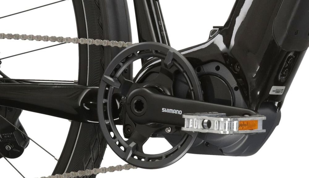 Zbliżenie na mechanizm napędowy roweru elektrycznego z widocznym napisem \'SHIMANO\' na korbie. Elementy są w kolorze czarnym z metalicznymi akcentami.