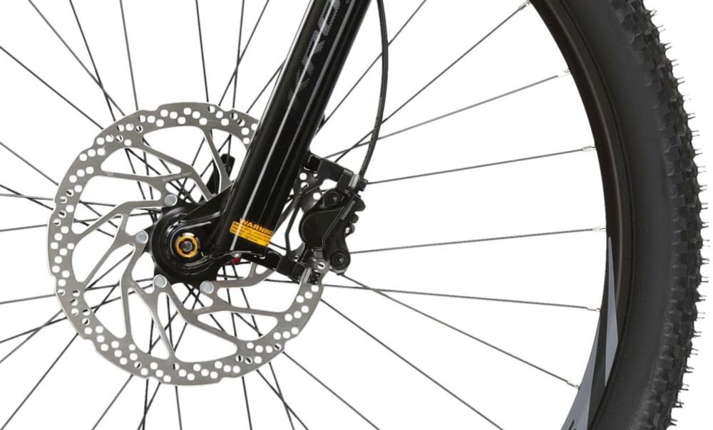Zbliżenie na tarczę hamulcową roweru z widocznym zaciskiem hamulcowym marki Shimano. W tle widać szprychy koła.
