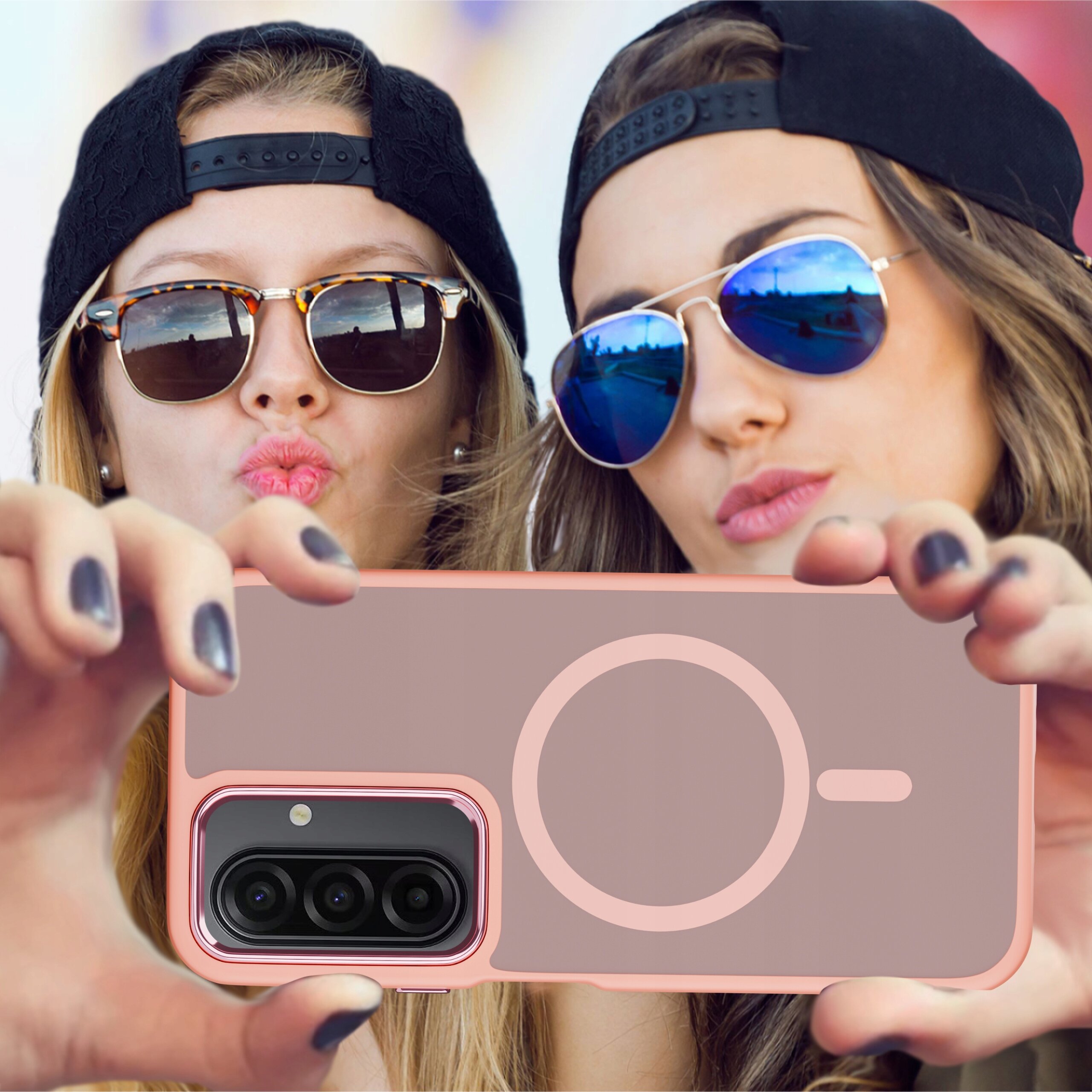 Dwie osoby w okularach przeciwsłonecznych i czapkach z daszkiem trzymają telefon w różowym etui z okrągłym wzorem i widocznym aparatem fotograficznym.