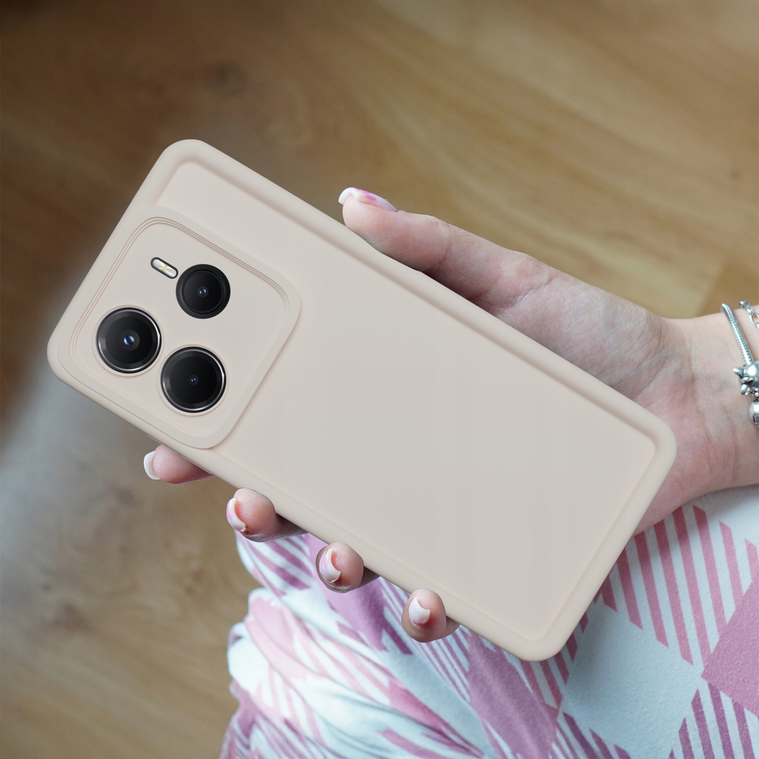 Osoba trzyma telefon w silikonowym, matowym etui, które jest w kolorze beżowym. Telefon posiada trzy widoczne obiektywy aparatu z tyłu.