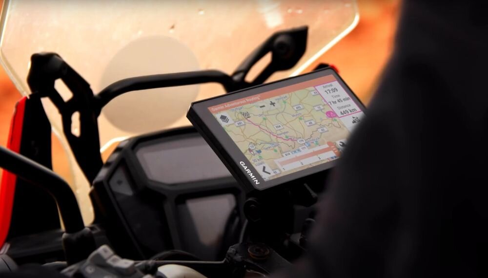 Na zdjęciu widać urządzenie nawigacyjne zamontowane na motocyklu, wyświetlające mapę z trasą i informacjami o odległości. Na obudowie urządzenia widoczny jest napis \'GARMIN\'.