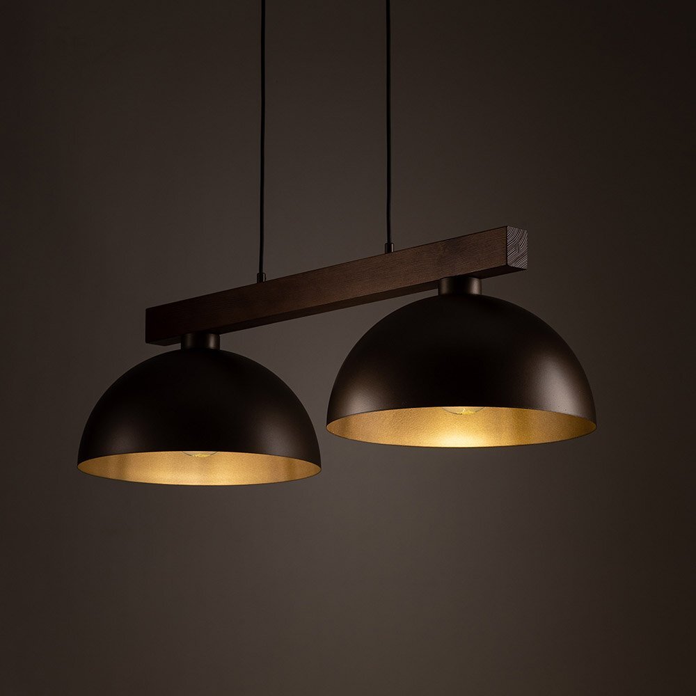 Lampa wisząca z dwoma półkulistymi kloszami w ciemnym kolorze, zawieszona na drewnianej belce, emitująca ciepłe światło.