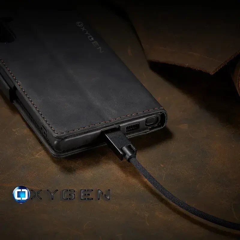 Czarny pokrowiec na telefon z logo \'OXYGEN\' jest podłączony do kabla. W tle widoczna jest ciemna powierzchnia.