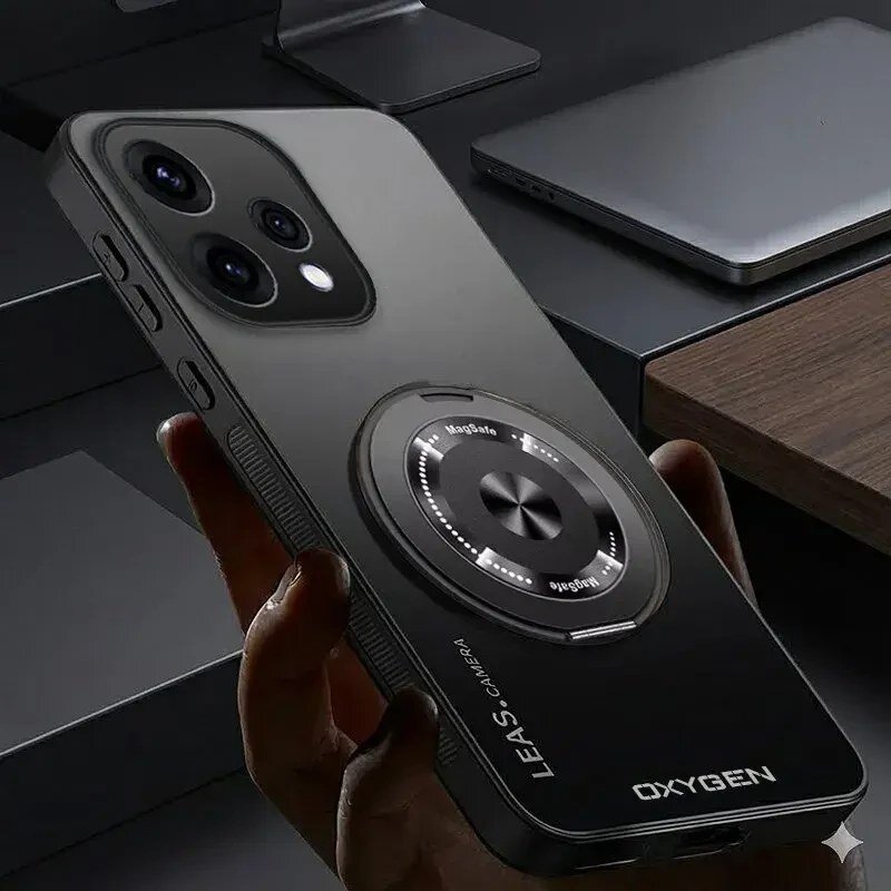 Czarny pokrowiec na telefon z napisem \'OXYGEN\' i \'LEaS-CAMERA\', posiada okrągły element z napisem \'MagSafe\'. W tle widoczne są elementy biurka, w tym laptop.