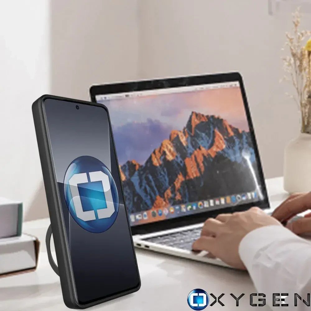 Na biurku stoi telefon w etui z logo OXYGEN, obok znajduje się otwarty laptop z widokiem na górski krajobraz na ekranie. W dolnym rogu widoczne jest logo OXYGEN.